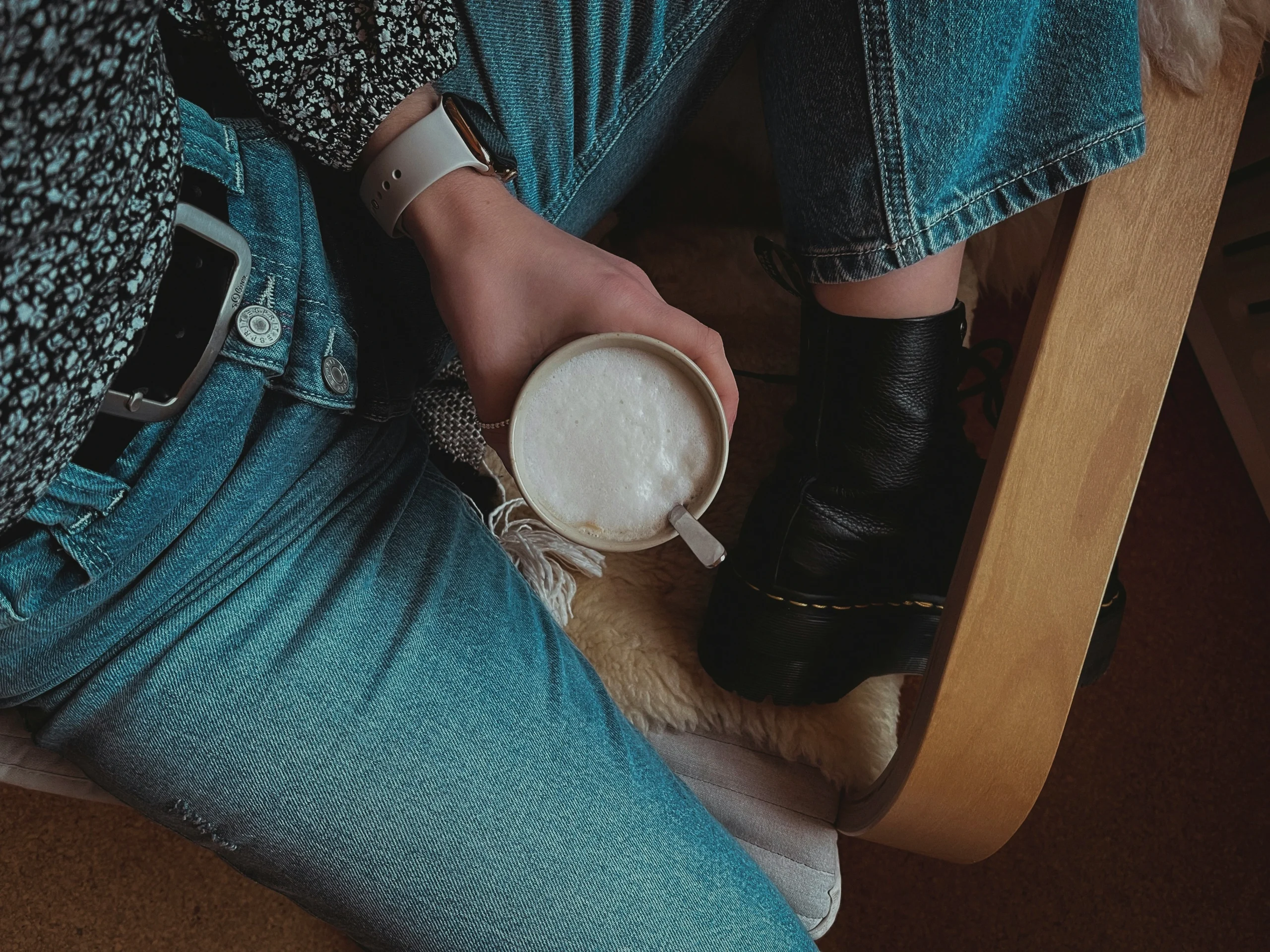 Overhead view of someone holding a latte while seated, wearing jeans and Doc Martens boots