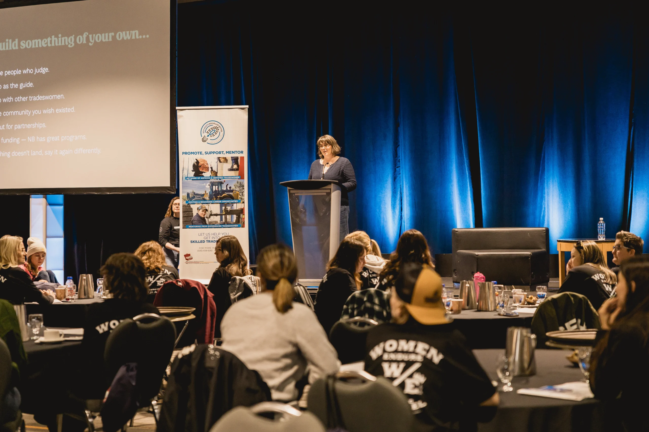 Erica Waddell speaking at a podium to a room of women in trades at a New Brunswick event