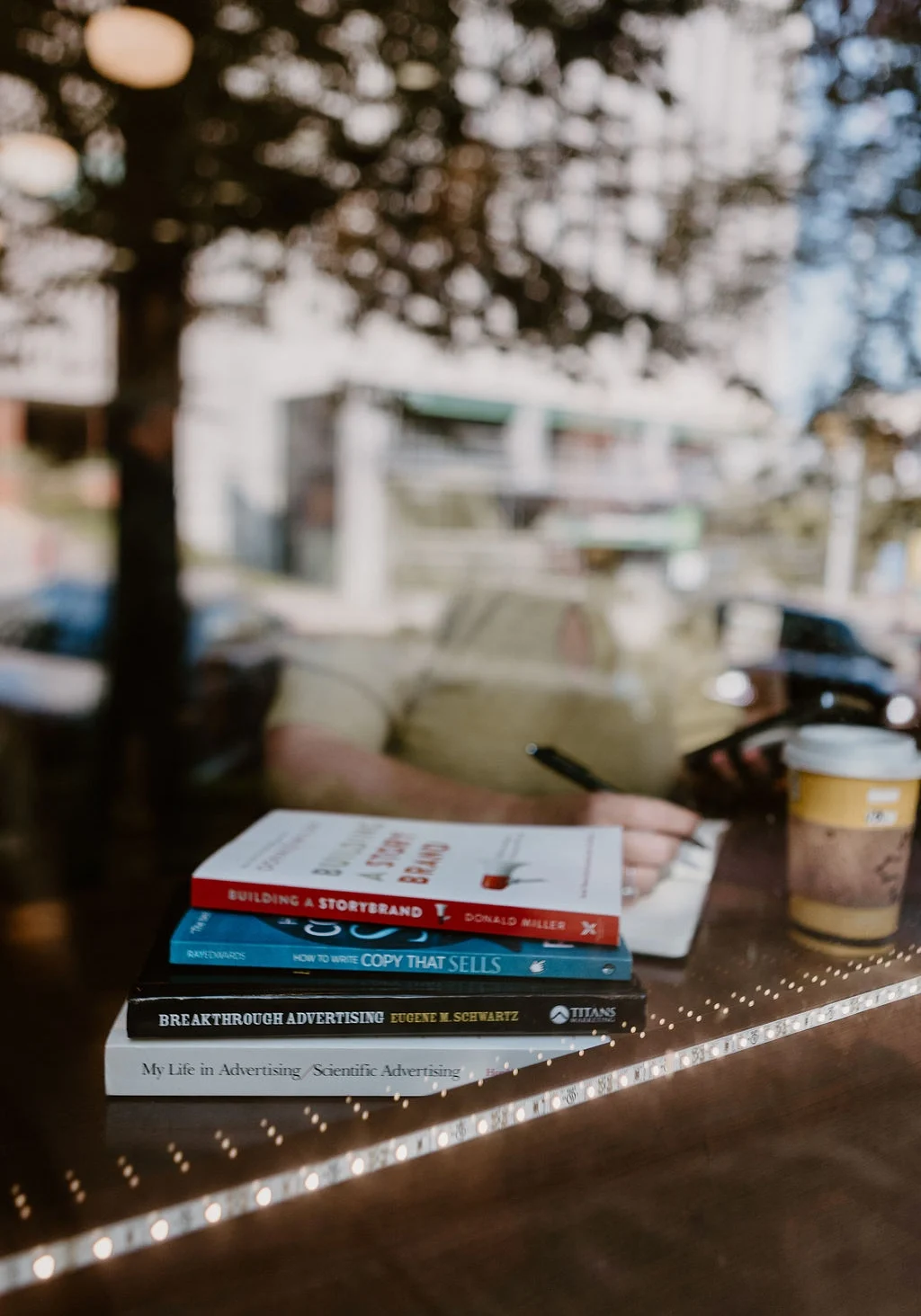 Stack of marketing books including Building a StoryBrand by Donald Miller and How to Write Copy That Sells by Ray Edwards, on a café table — the reading list behind Post Road Marketing's approach to brand messaging for women entrepreneurs