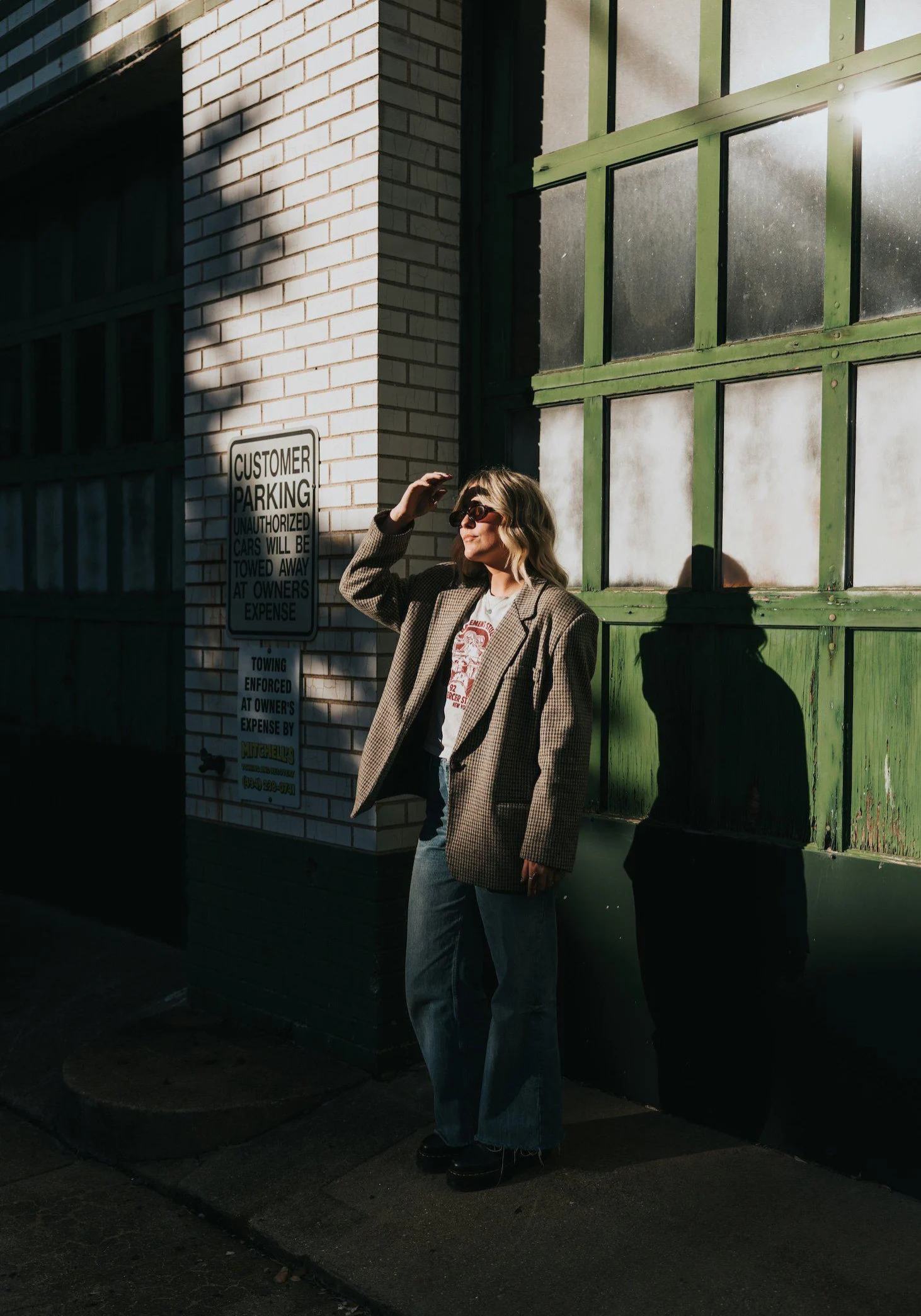 Woman in an oversized blazer and sunglasses standing on an urban street in bright sunlight