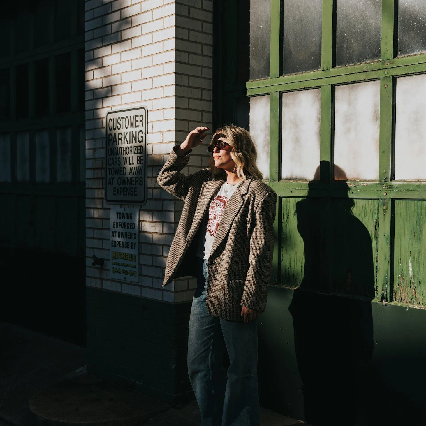 Woman in an oversized blazer and sunglasses standing on an urban street in bright sunlight